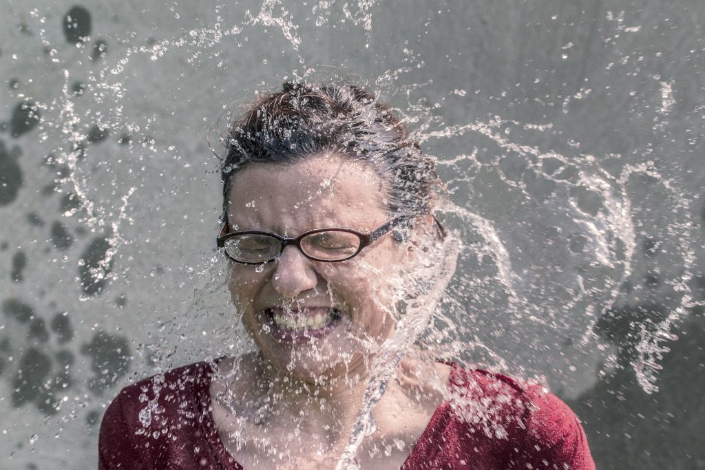 woman wearing glasses being splashed in the face with water