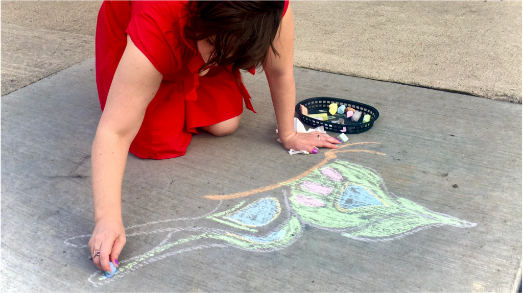 Person in a red dress drawing a butterfly on a sidewalk with chalk